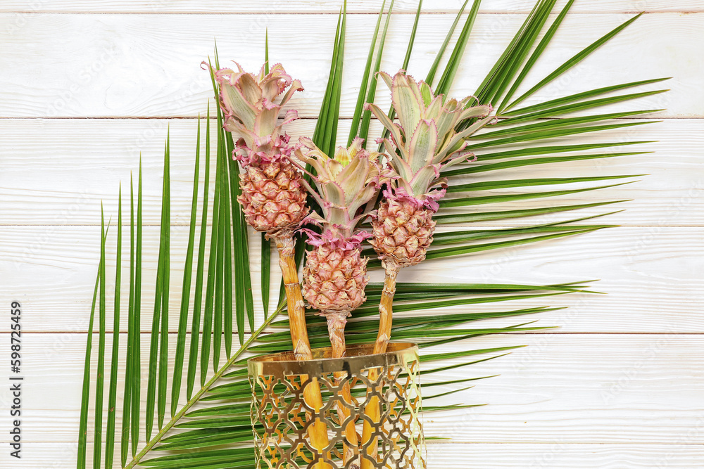 Vase with decorative pineapples and palm leaf on white wooden background