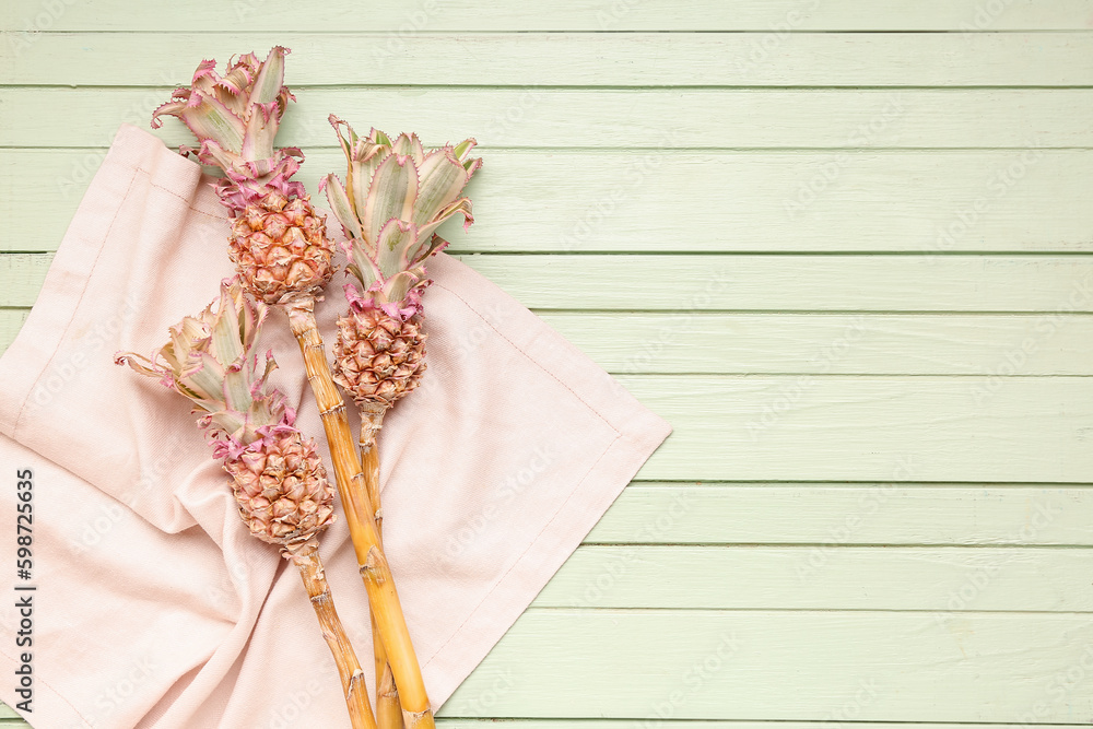 Decorative pineapples with napkin on green wooden background