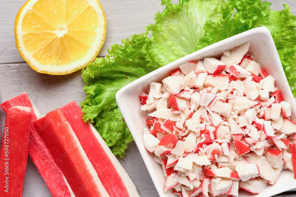 Bowl with tasty chopped crab sticks on light wooden background, closeup