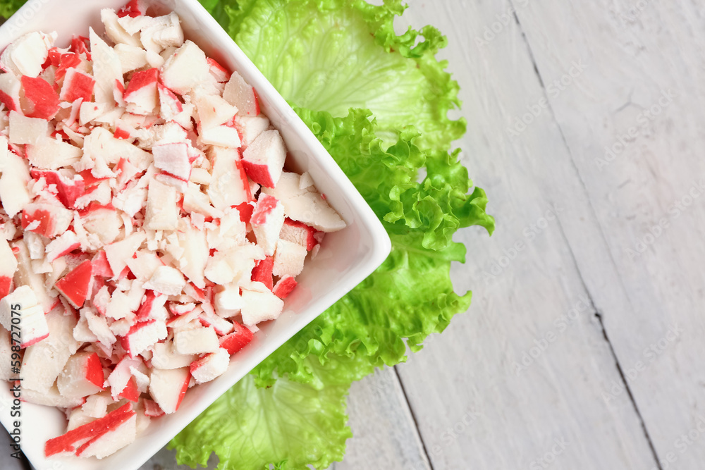 Bowl with tasty chopped crab sticks on light wooden background, closeup