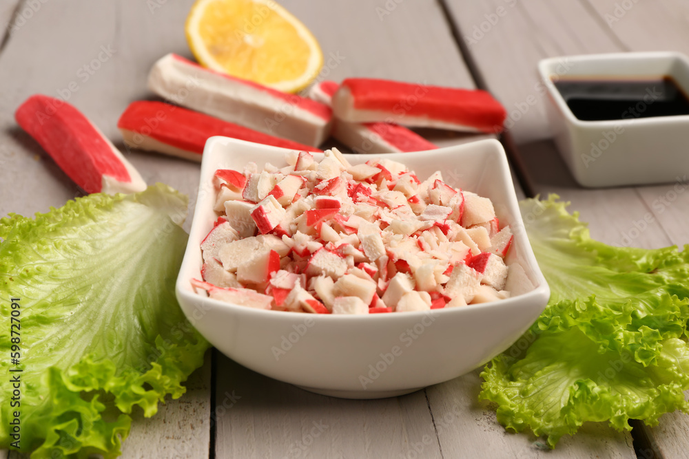 Bowl with tasty chopped crab sticks on light wooden background