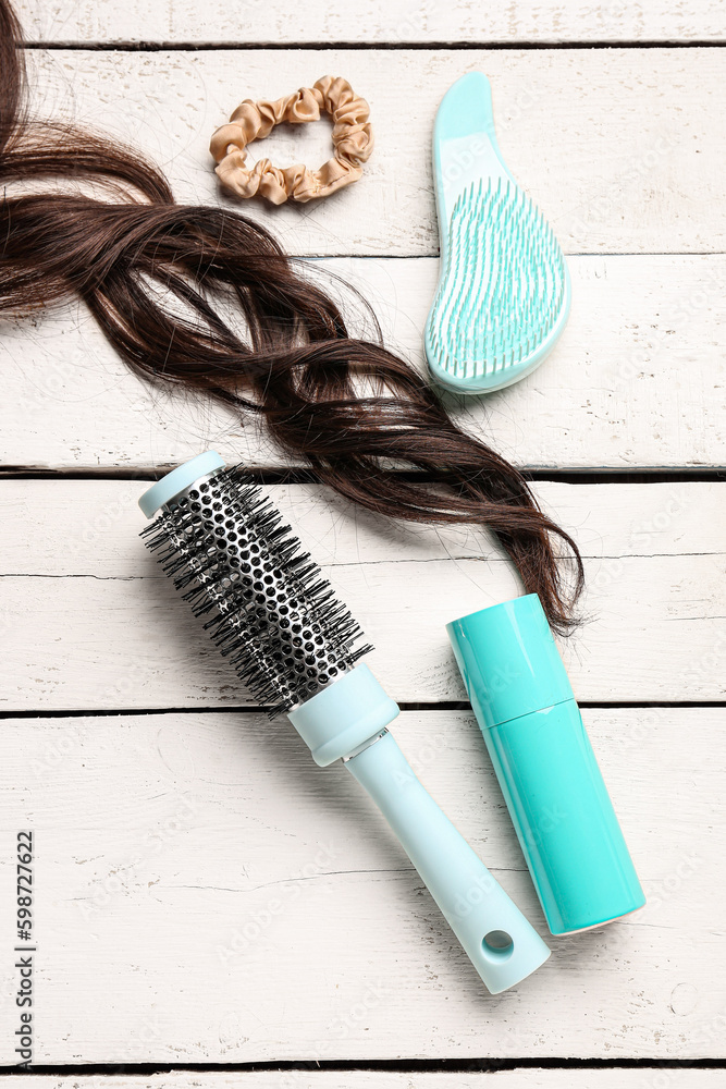 Curly brown hair with brushes, spray and scrunchy on white wooden background