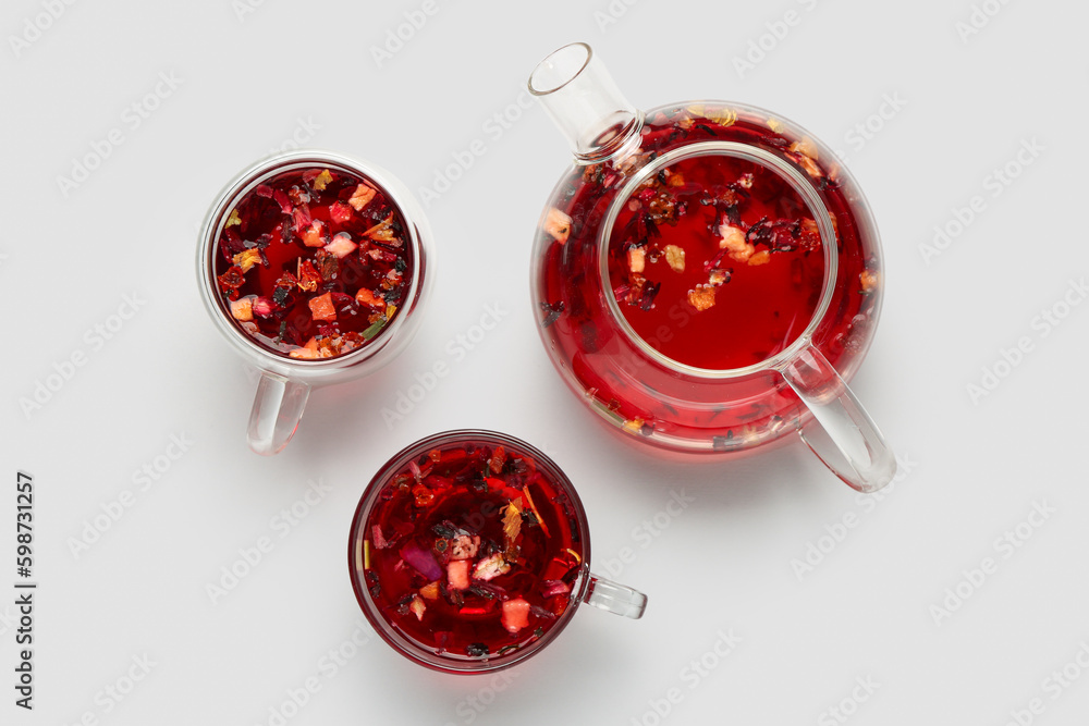 Transparent teapot with cups of fruit tea on grey background