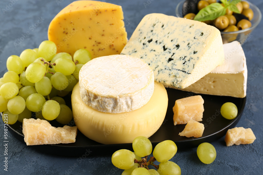 Plate with different types of cheese and grapes on blue background