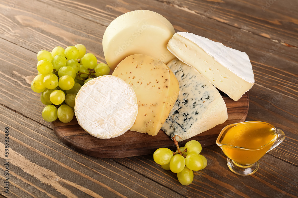 Board with different types of cheese, honey and grapes on wooden background