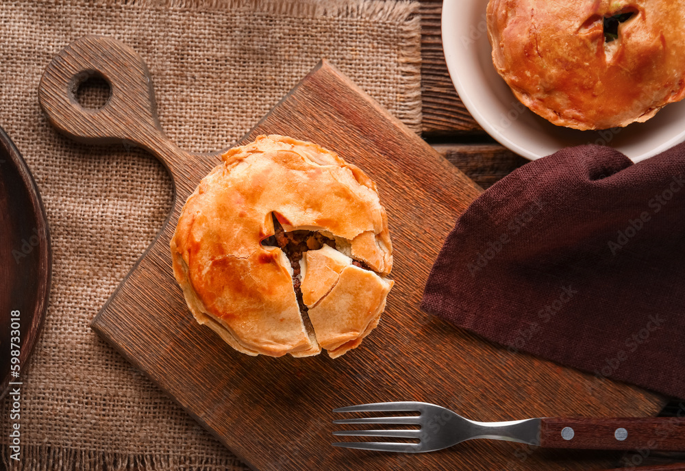 Wooden board with tasty meat pot pies on table