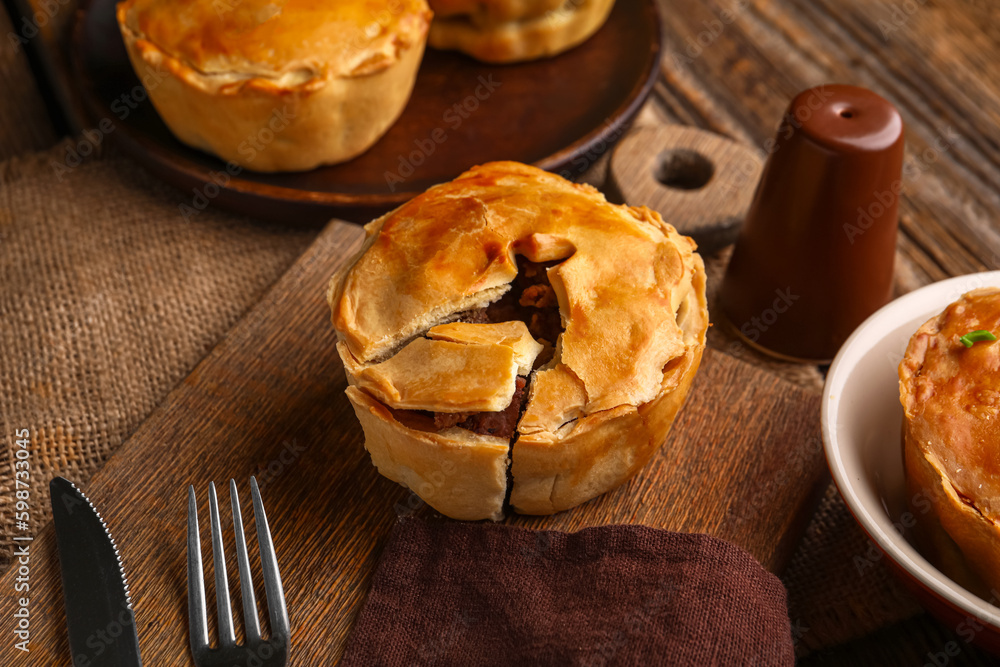 Wooden board with tasty meat pot pie on table