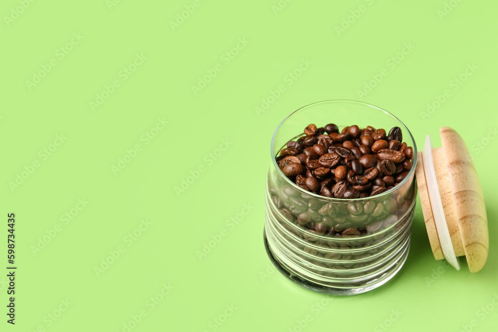 Glass jar with coffee beans on green background