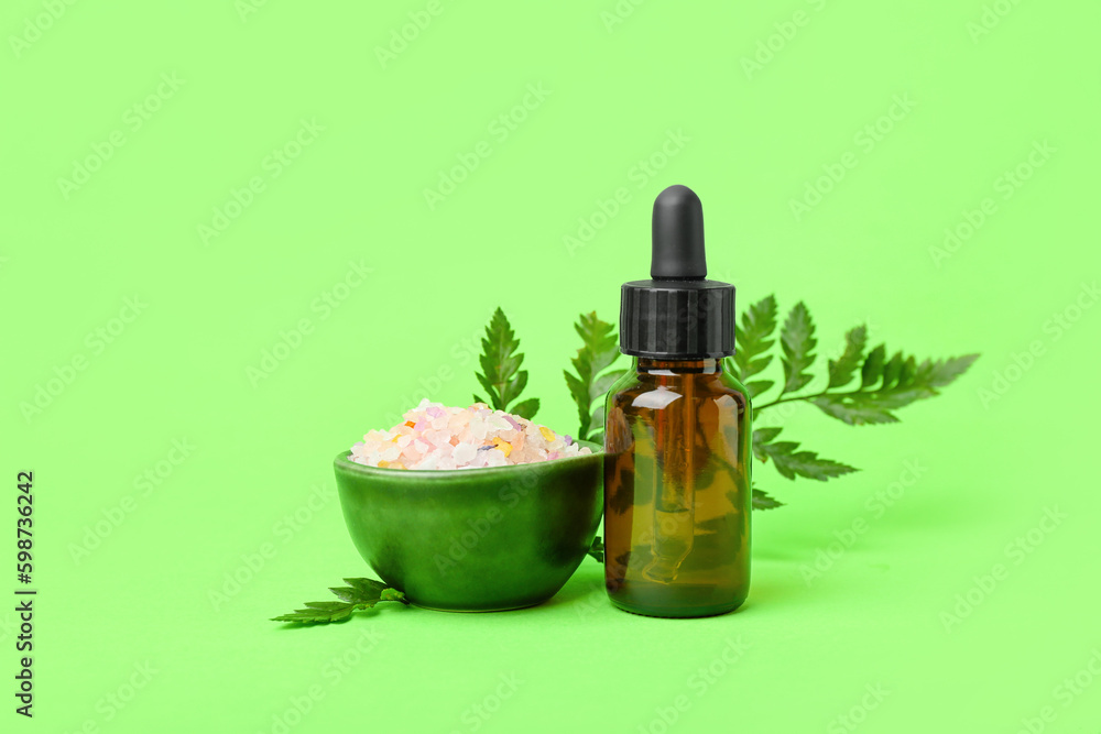 Bottle of cosmetic oil with plant twig and sea salt on light green background