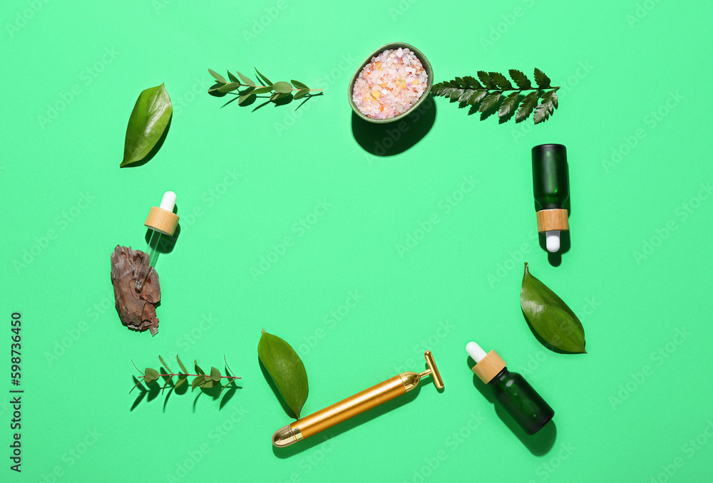 Frame made of bottles with cosmetic oil and leaves on green background