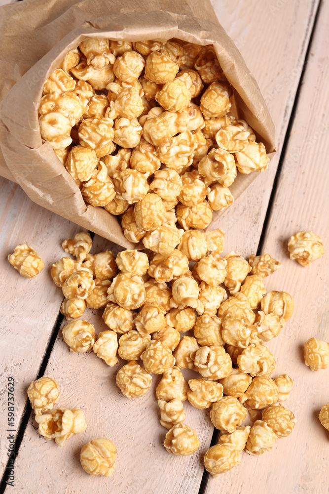 Paper bag with crispy popcorn on white wooden background