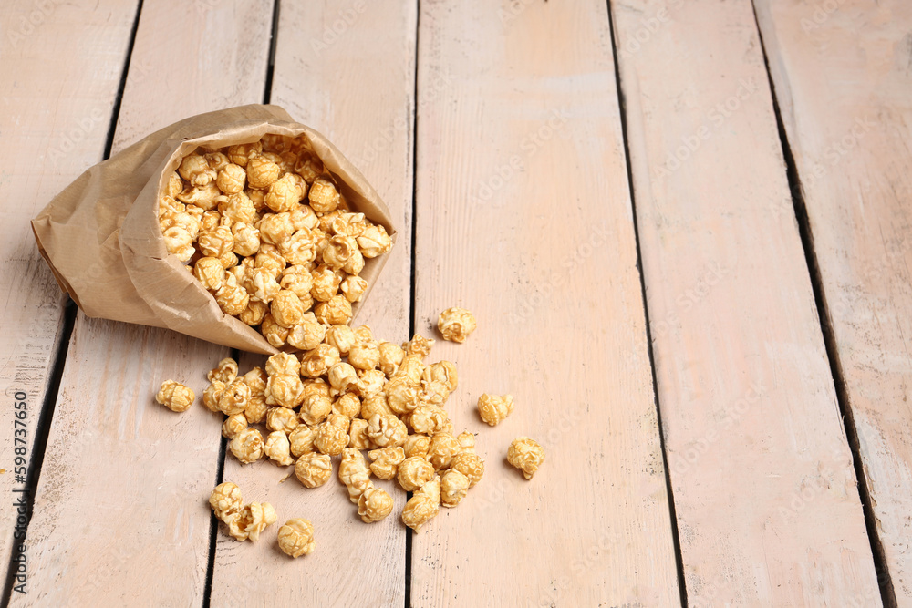 Paper bag with crispy popcorn on white wooden background