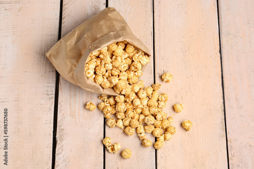 Paper bag with crispy popcorn on white wooden background