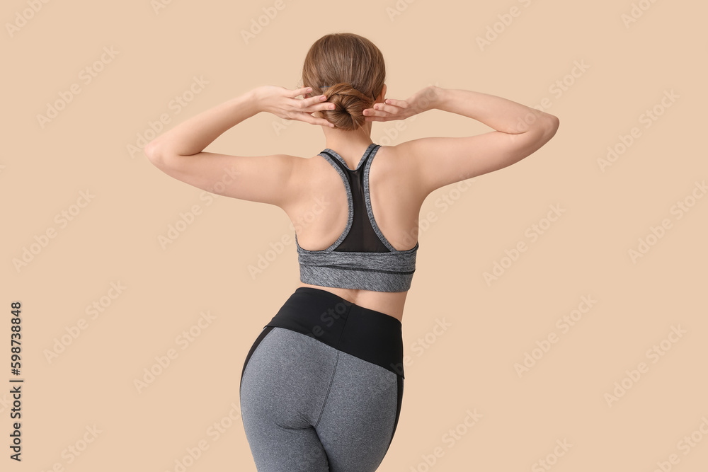 Young woman in sportswear on beige background, back view