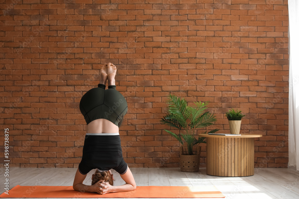 Sporty young woman doing headstand while practicing yoga  at home