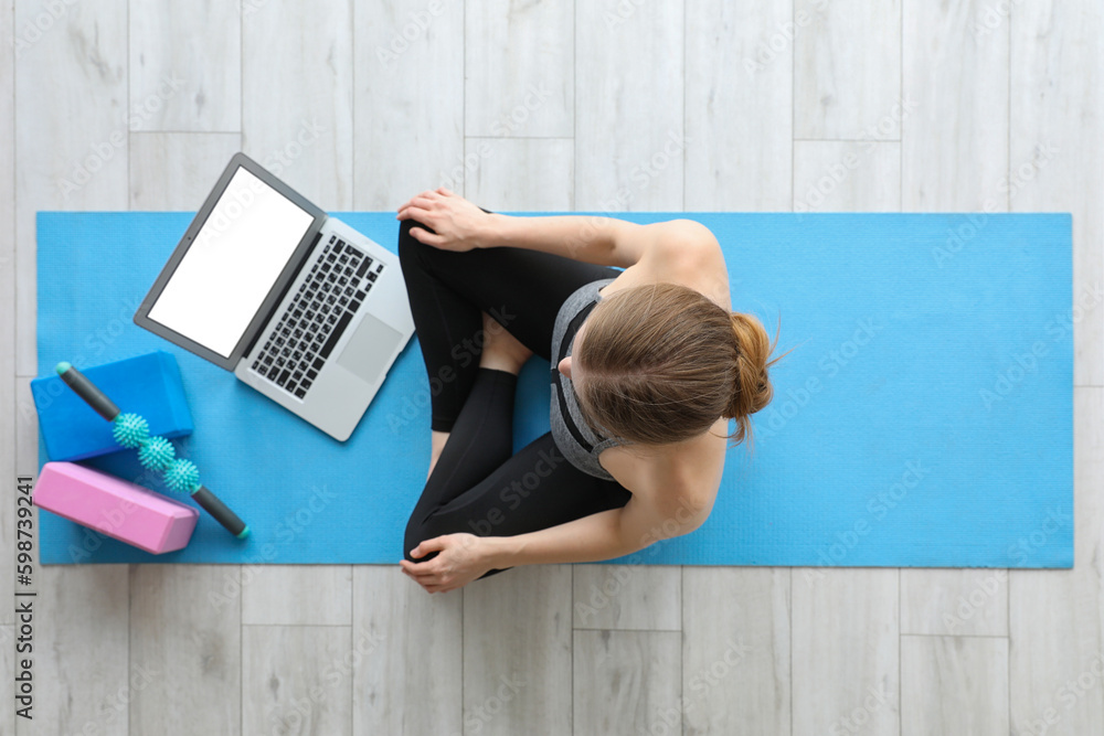 Sporty young woman with laptop doing yoga in gym, top view