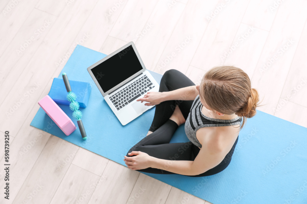 Sporty young woman with laptop doing yoga in gym