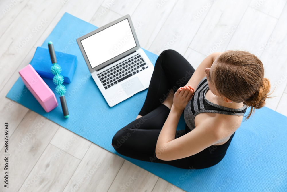 Sporty young woman with laptop doing yoga in gym