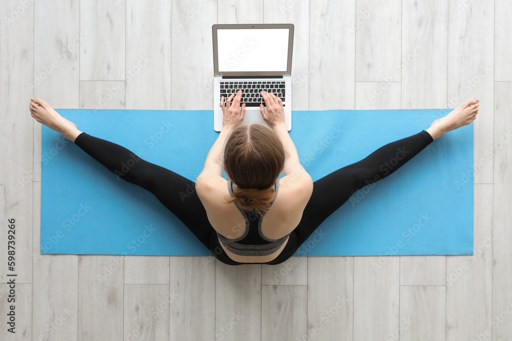 Sporty young woman with laptop doing yoga in gym, top view