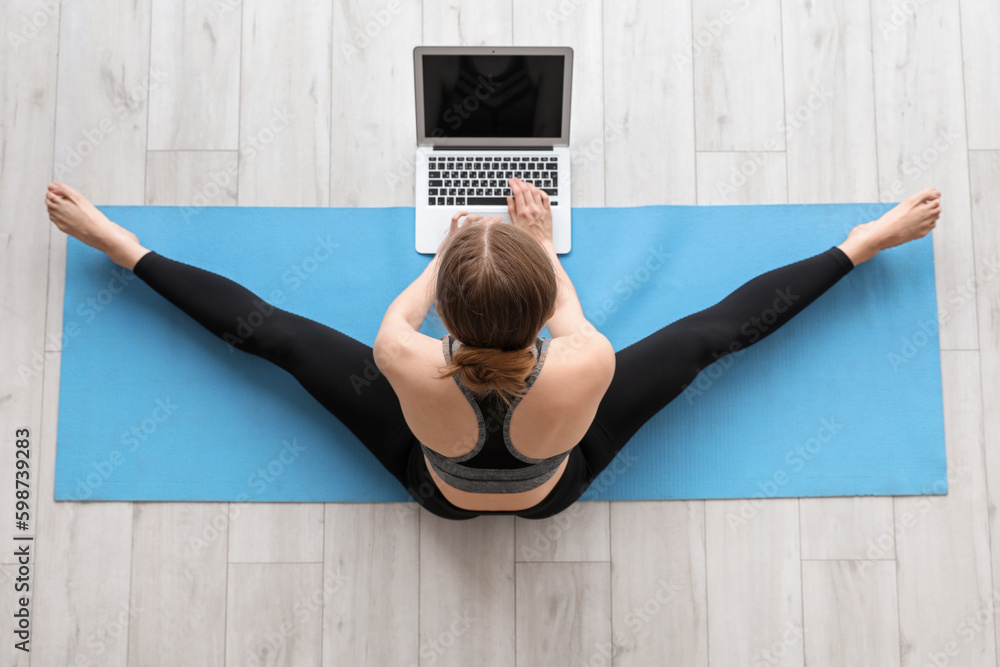 Sporty young woman with laptop doing yoga in gym, top view