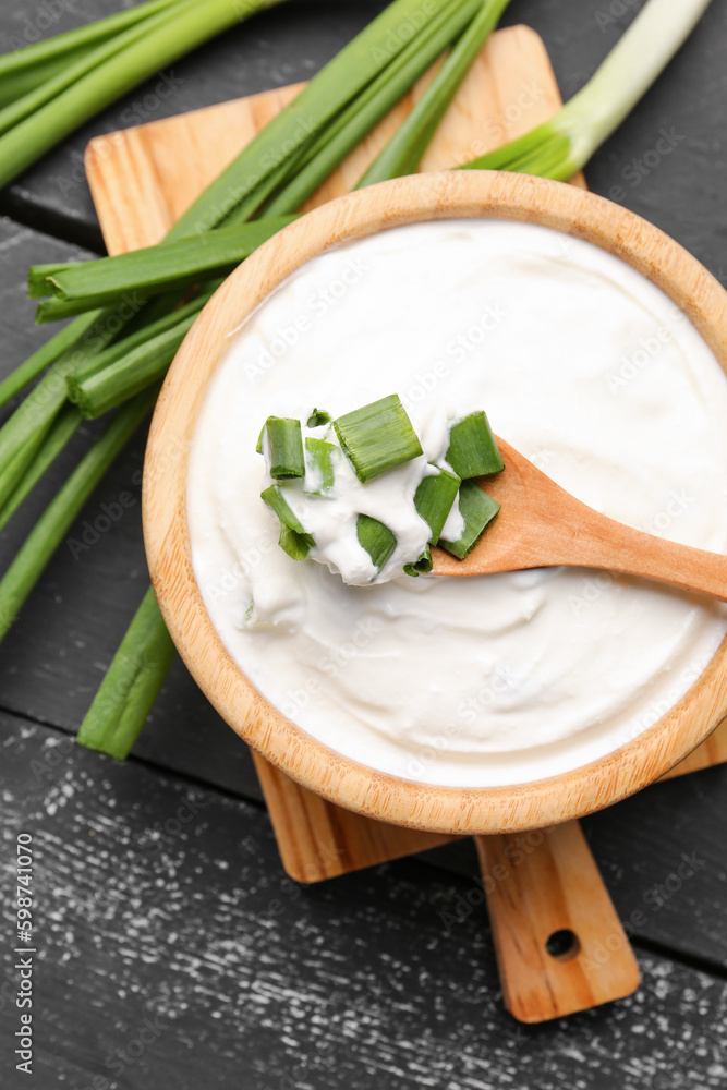 Bowl of tasty sour cream with green onion on dark wooden background, closeup