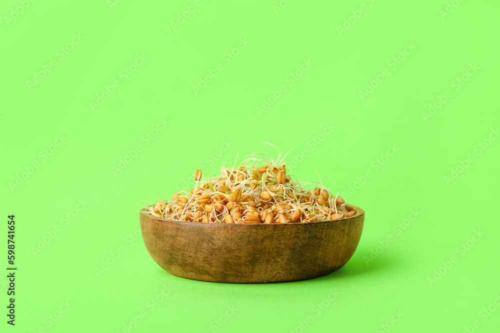 Wooden bowl with sprouted wheat on light green background