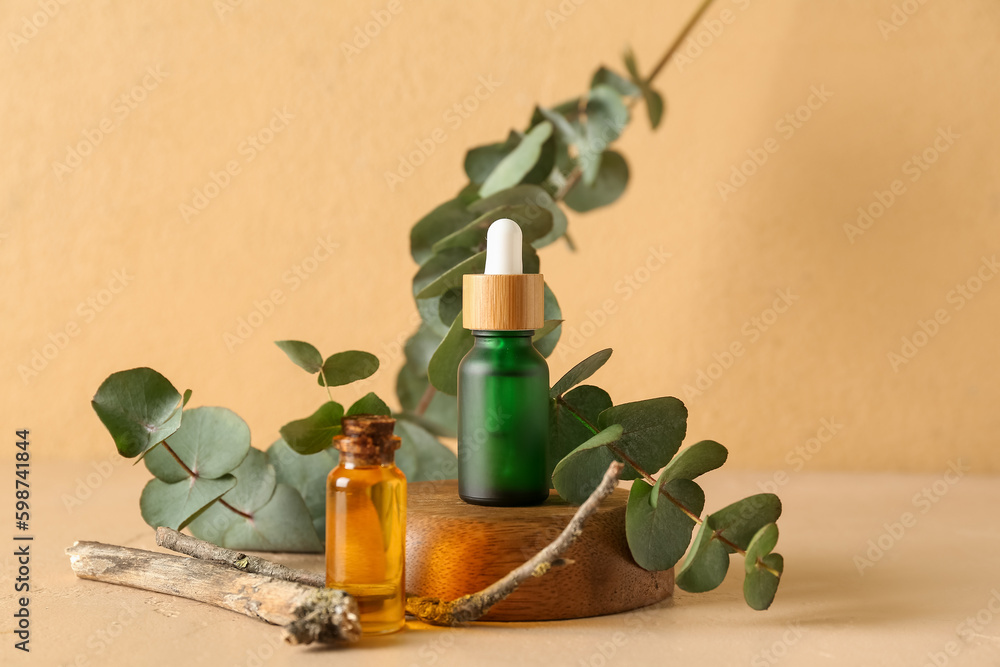 Bottles of cosmetic oil with eucalyptus branch on orange background