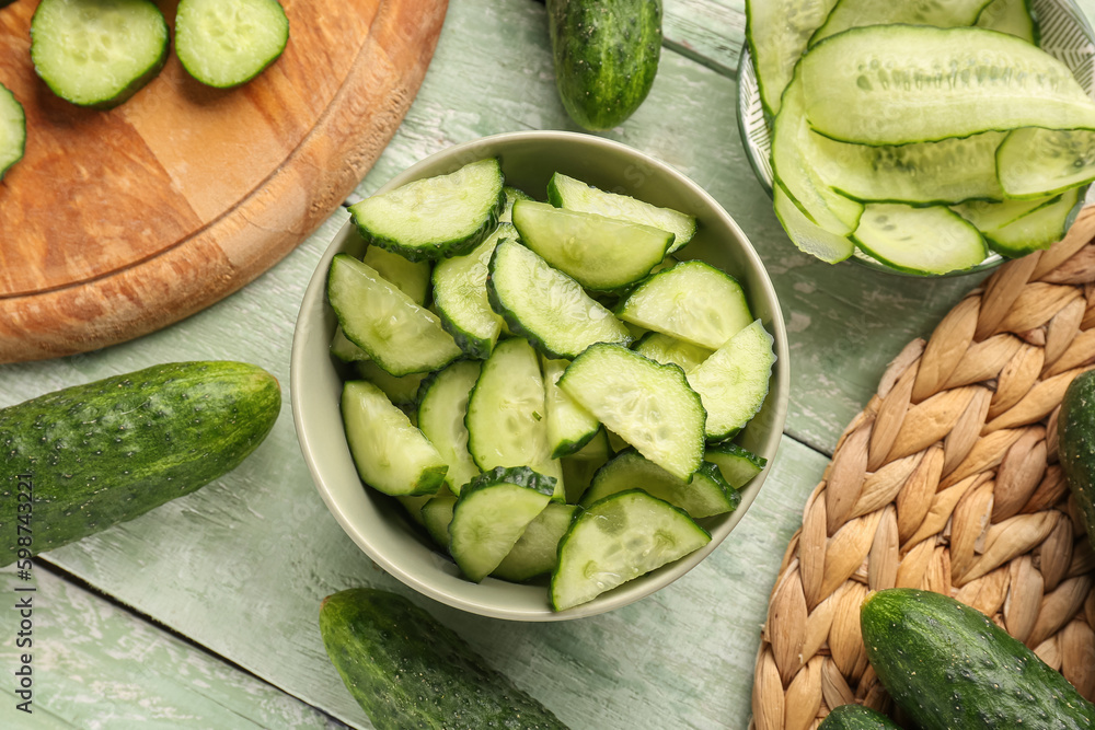 Bowl with pieces of fresh cucumber on light wooden background