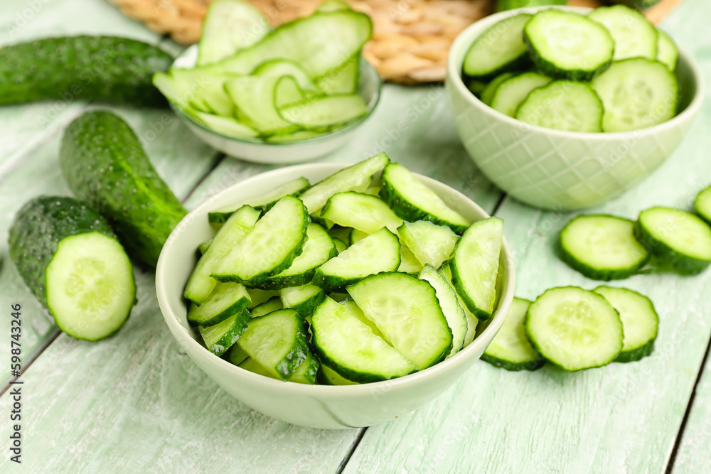 Bowl with pieces of fresh cucumber on light wooden background