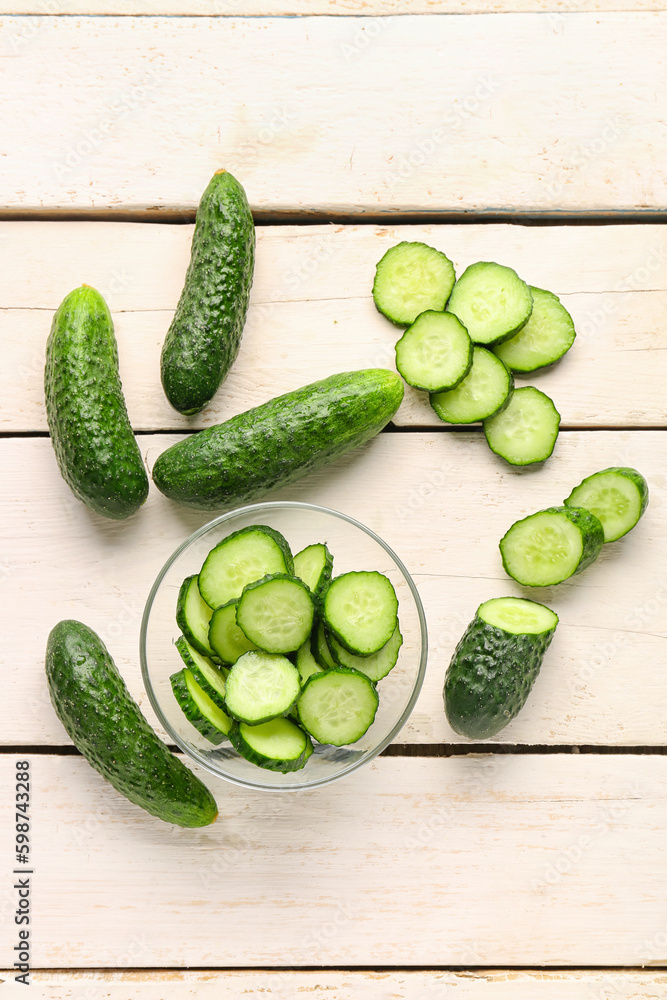 Bowl with fresh cut cucumbers on light wooden background