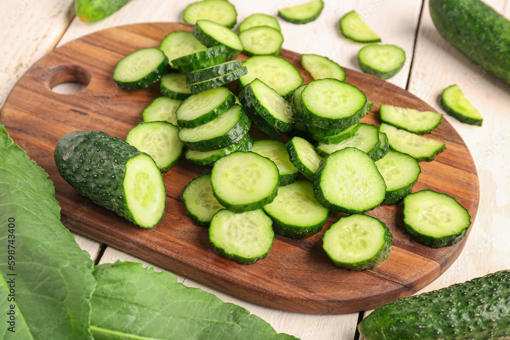 Wooden board with pieces of fresh cucumber on table