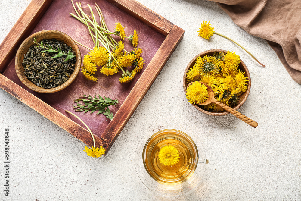 Glass cup of healthy dandelion tea and bowl with flowers on white background