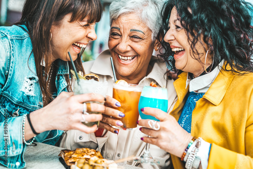 Happy senior women drinking cocktail glasses sitting at bar table - Group of best friends enjoying h