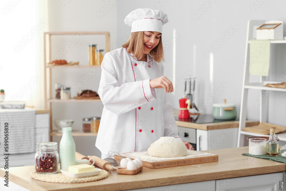 Female baker sprinkling dough with flour at table in kitchen