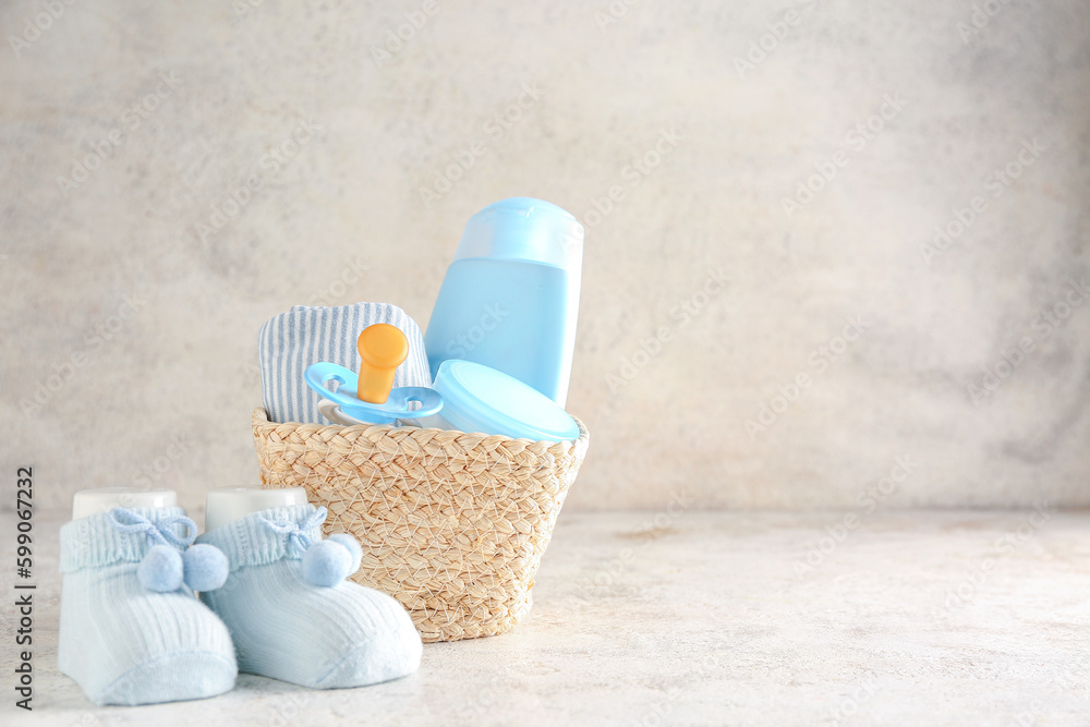 Basket with baby clothes, pacifier, cosmetics and socks on light background