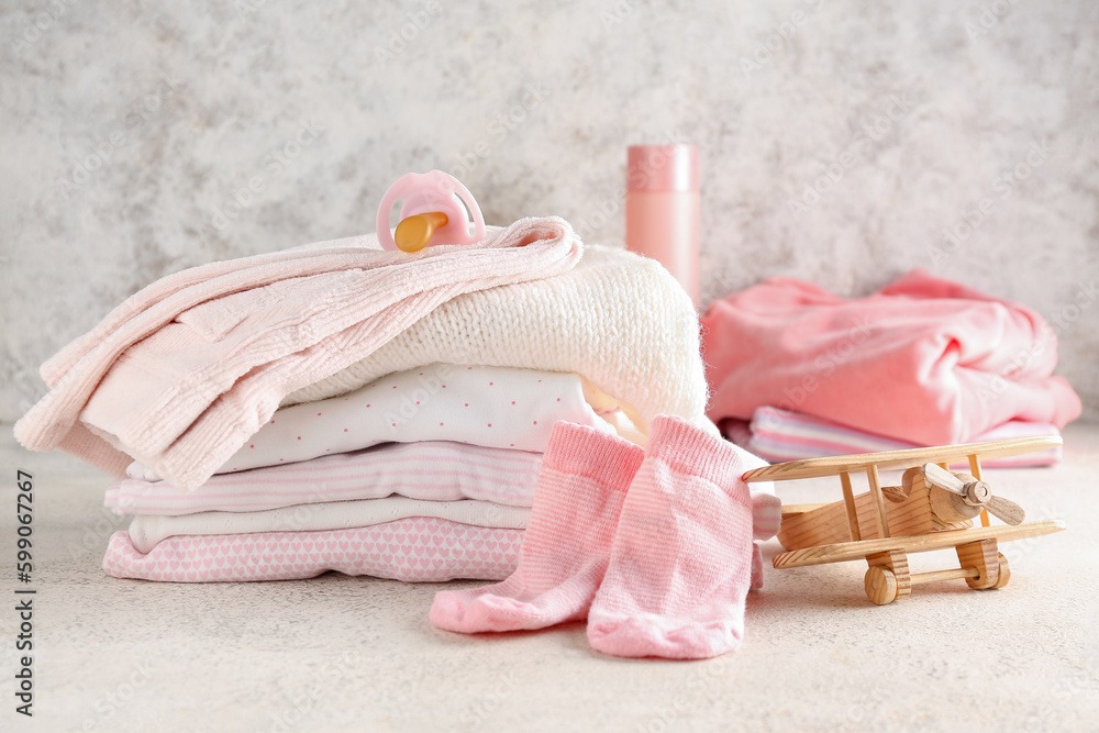 Stack of baby clothes, pacifier and wooden plane on light background