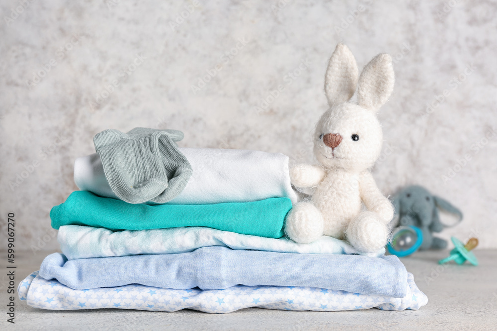 Stack of baby clothes and toy bunny on light background