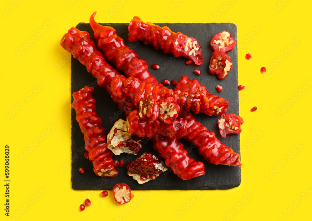 Slate board with tasty churchkhela and pomegranate on yellow background