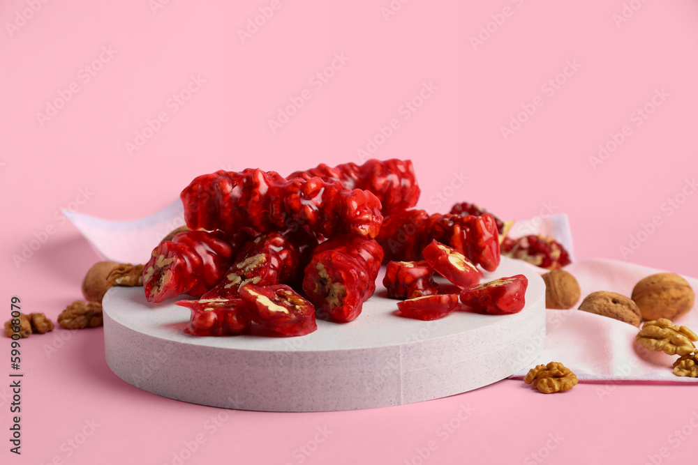 Board with tasty churchkhela and nuts on pink background