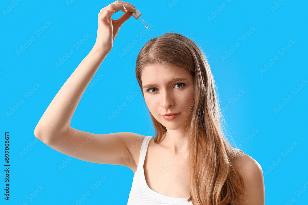 Young woman using serum for hair growth on blue background