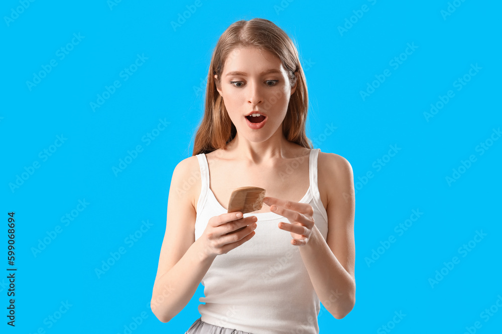 Shocked young woman with comb and fallen down hair on blue background