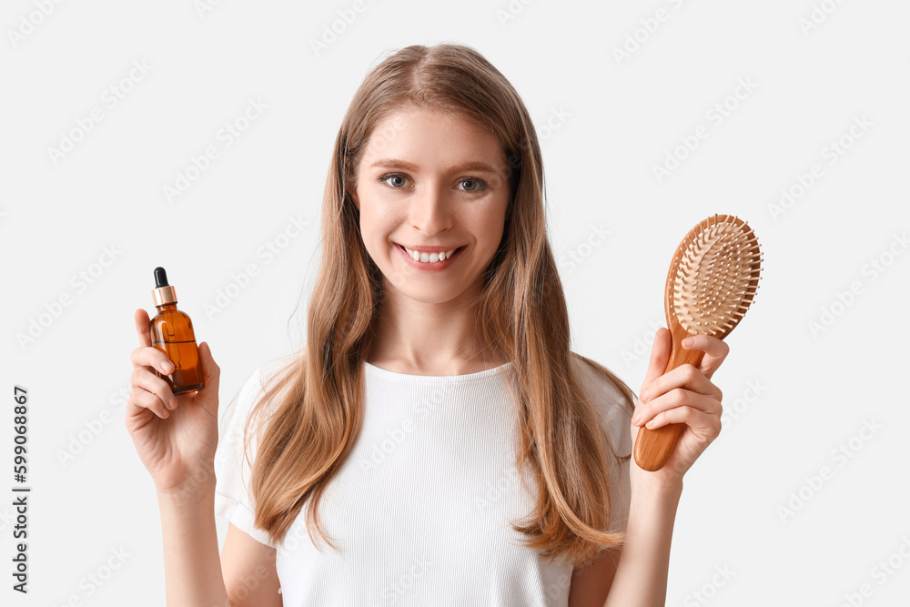 Young woman with serum for hair growth and brush on light background