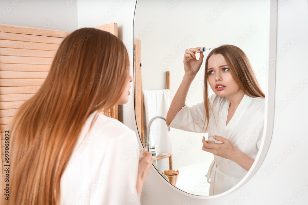 Young woman using serum for hair loss treatment at home