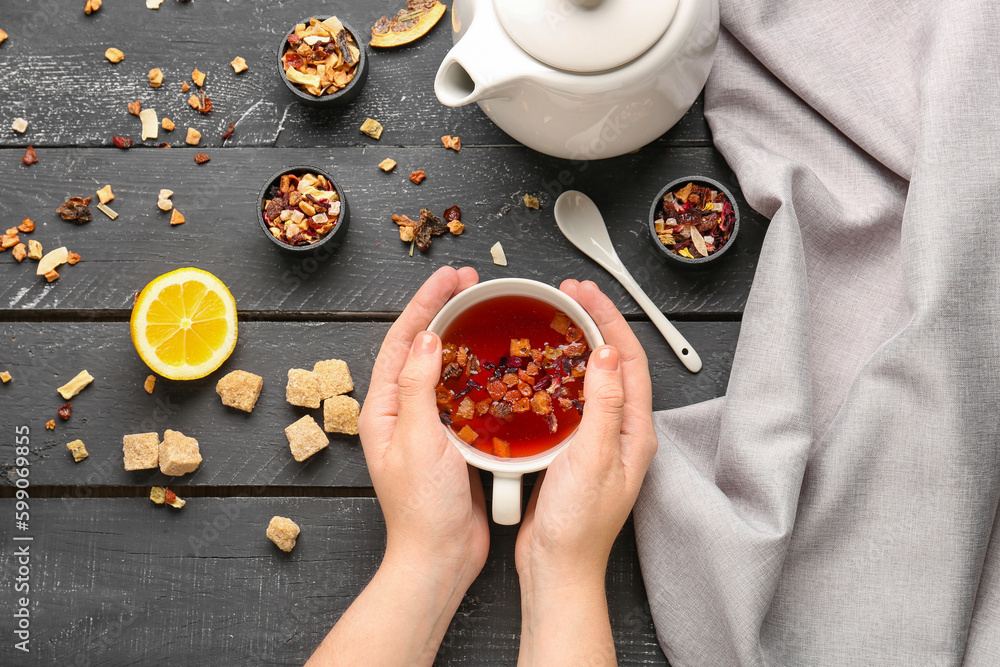 Composition with woman holding cup of hot fruit tea on black wooden table