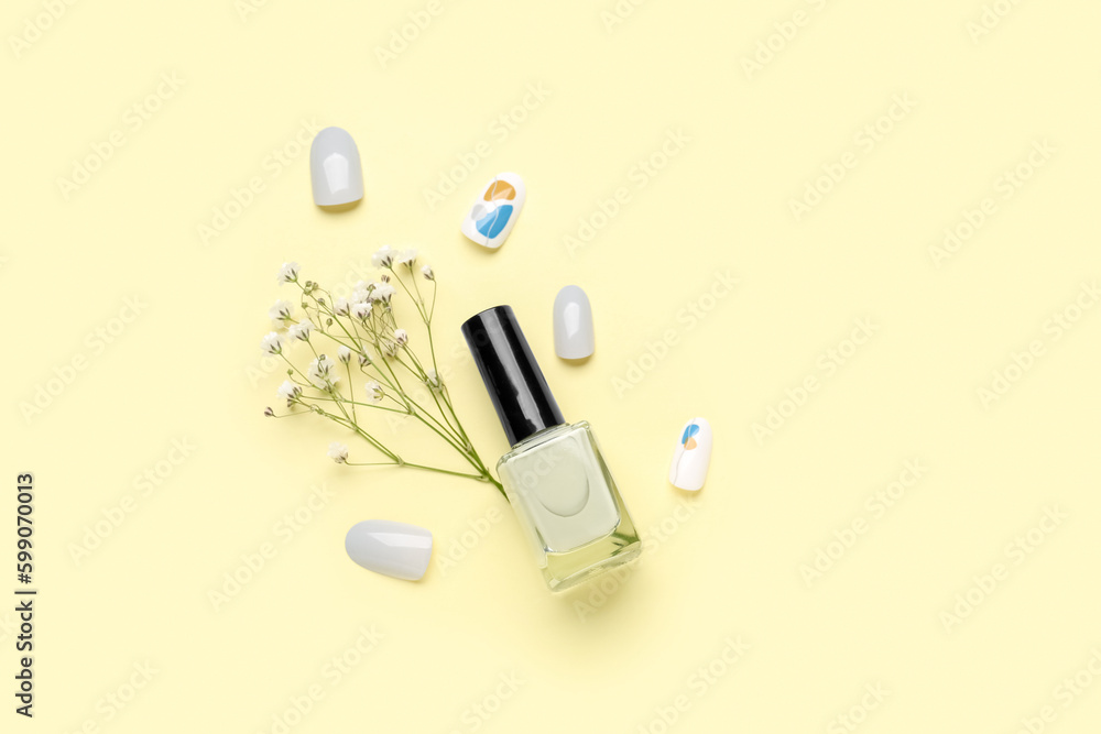 Press-on nails with polish and flowers on yellow background