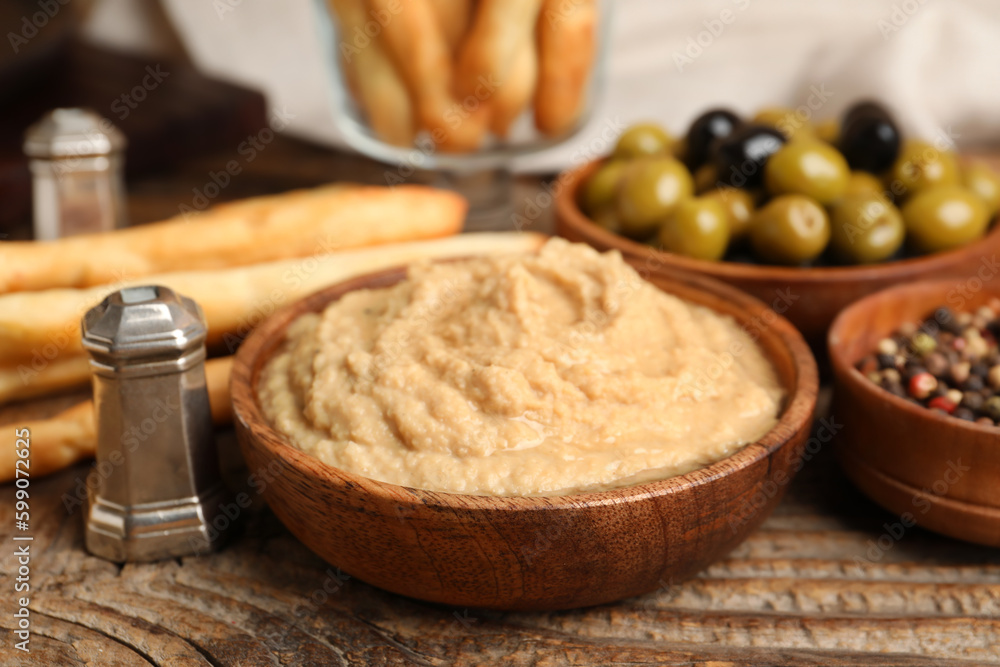 Bowl with tasty hummus on wooden background, closeup