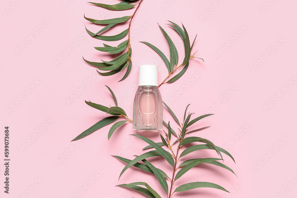 Bottle of micellar water with plant branches on pink background