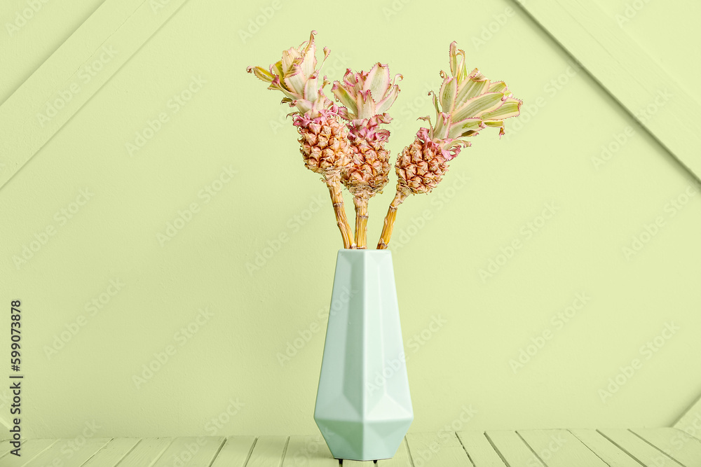 Vase with decorative pineapples on table near green wall