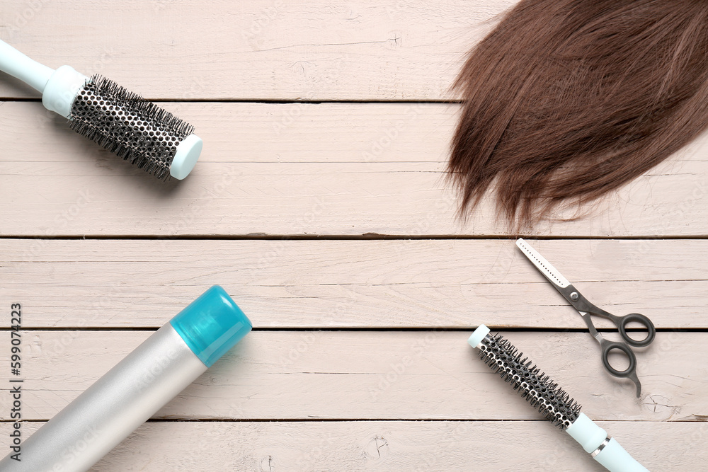 Frame made of brown hair with brushes, spray and scissors on white wooden background