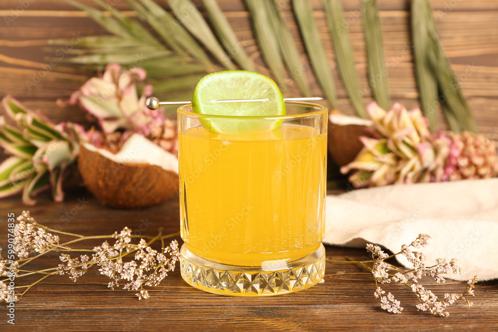 Glass of cocktail with lime and flowers on wooden table, closeup